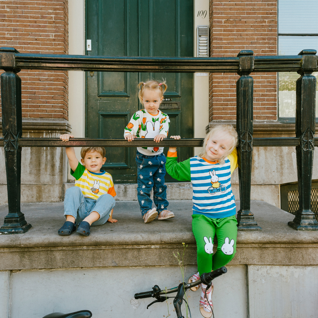 Niño con el conjunto de bambú «Move» de {{5acda3a9b3eeac56b7846cf24e8ac4d8}, compuesto por una sudadera con motivo de bicicleta y unos pantalones de chándal verdes.