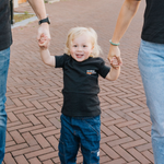 Child holding hands with two adults on a brick pathway